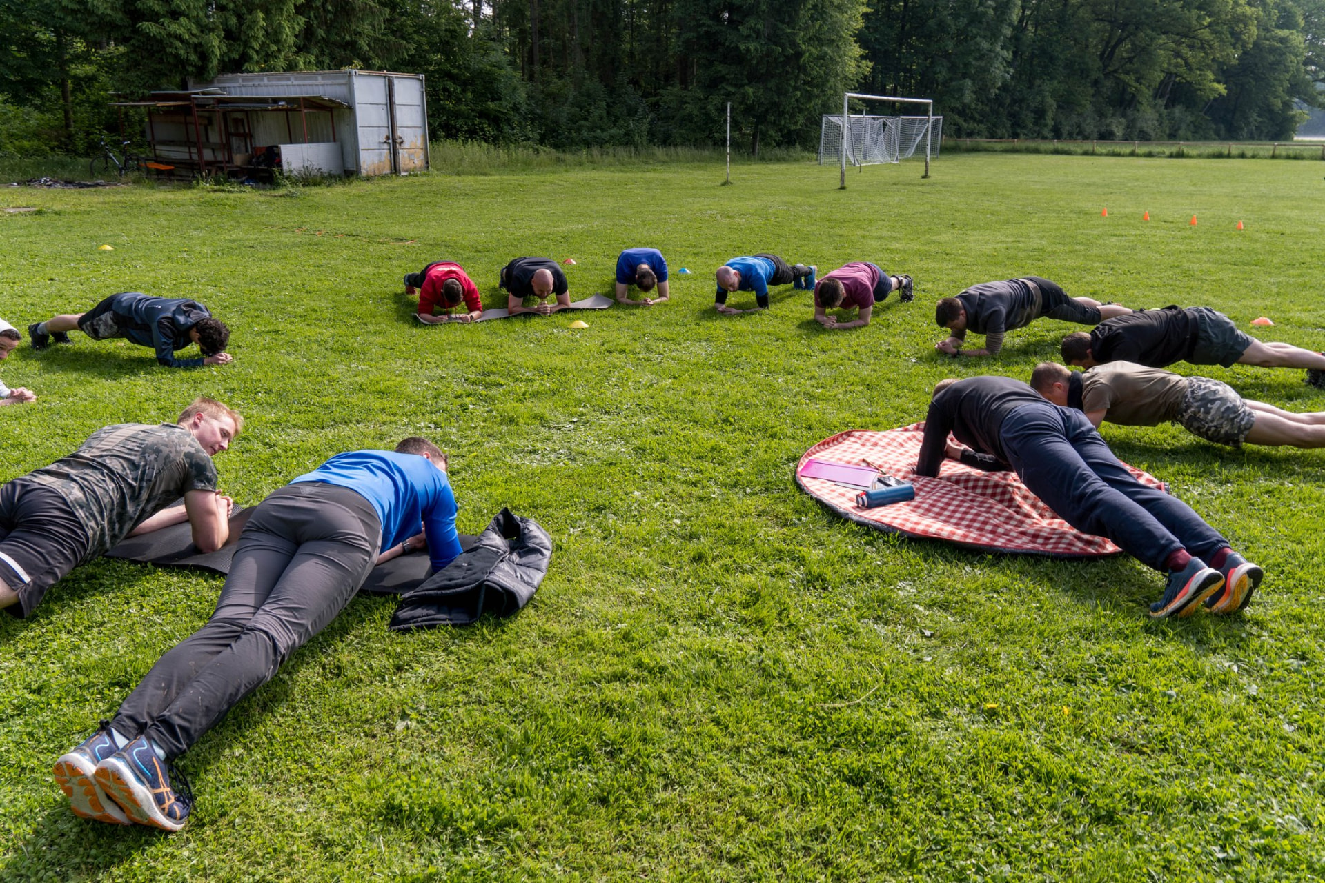 Skupina udeležencev izvaja plank na travniku